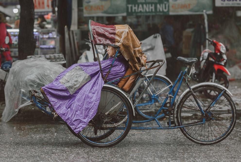 A cyclo driver staying in the rain and tiredly waiting for a customer