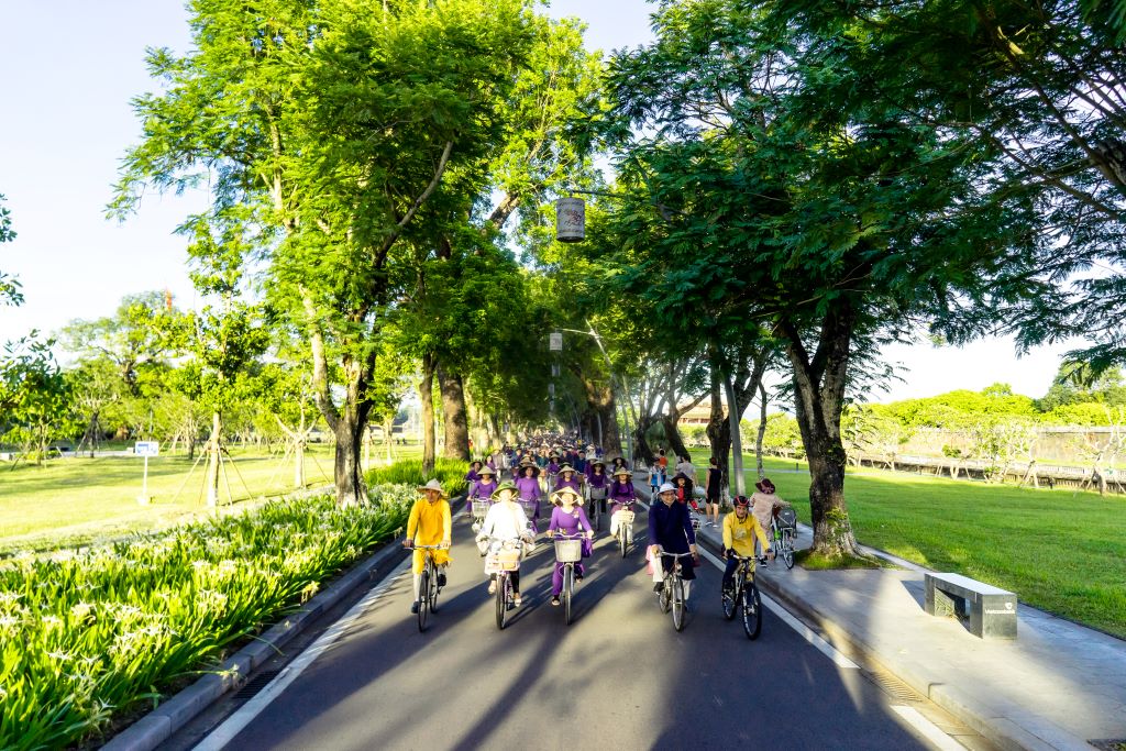 A poetic scene of people dressing in ao dai and riding under shaded streets